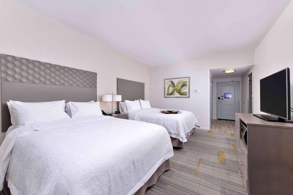 Une chambre d’hôtel avec deux lits, une télévision, un bureau et une porte donnant sur une salle de bain.