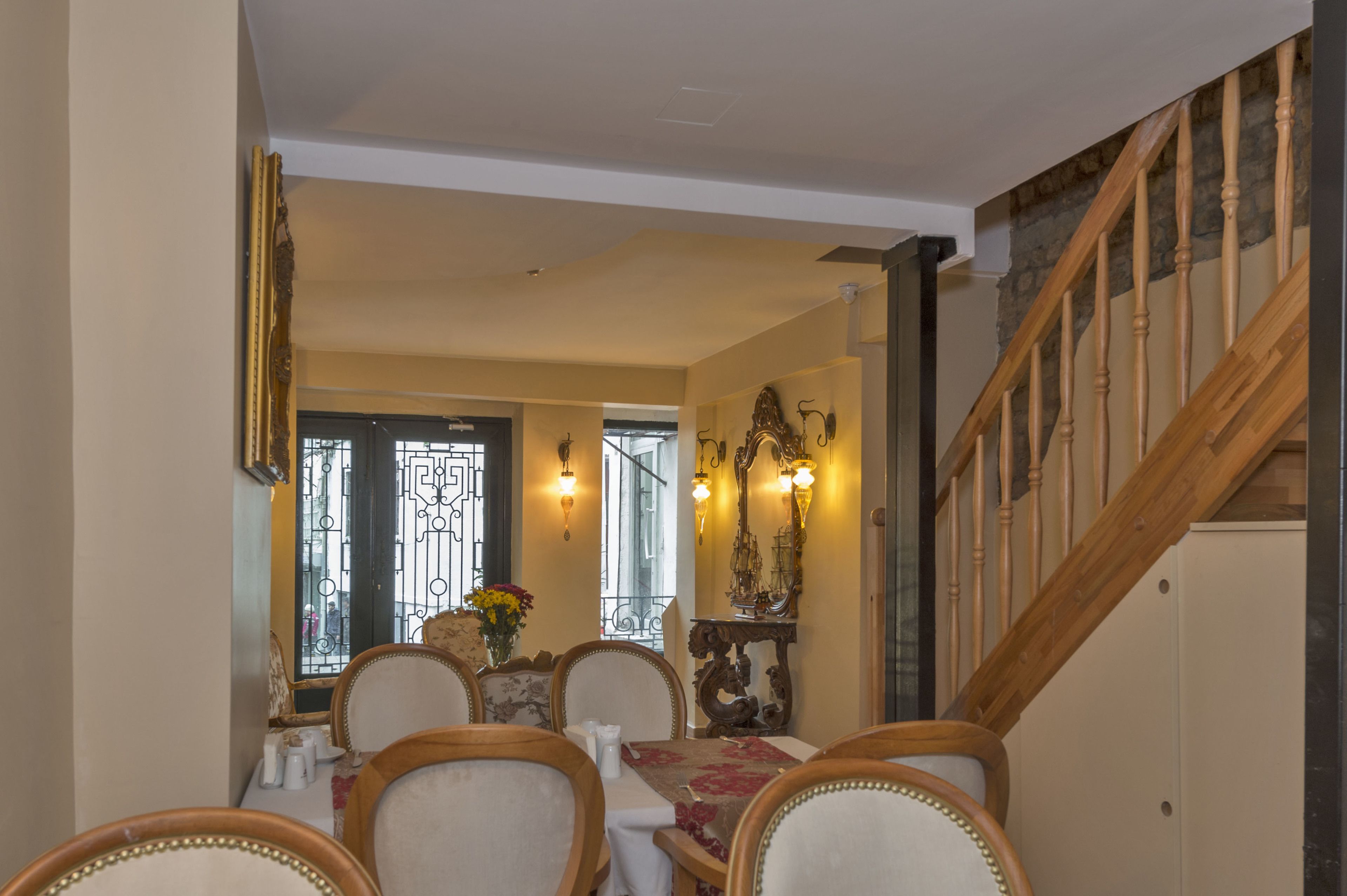 A dining area with a table set for four, chairs with wooden frames, a decorative mirror, and a staircase with wooden railings.