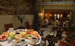 A dining area with a variety of breakfast items on a table, surrounded by chairs and tables, with a stone wall and indoor lighting. - By Murat Royal Hotels (Istanbul)
