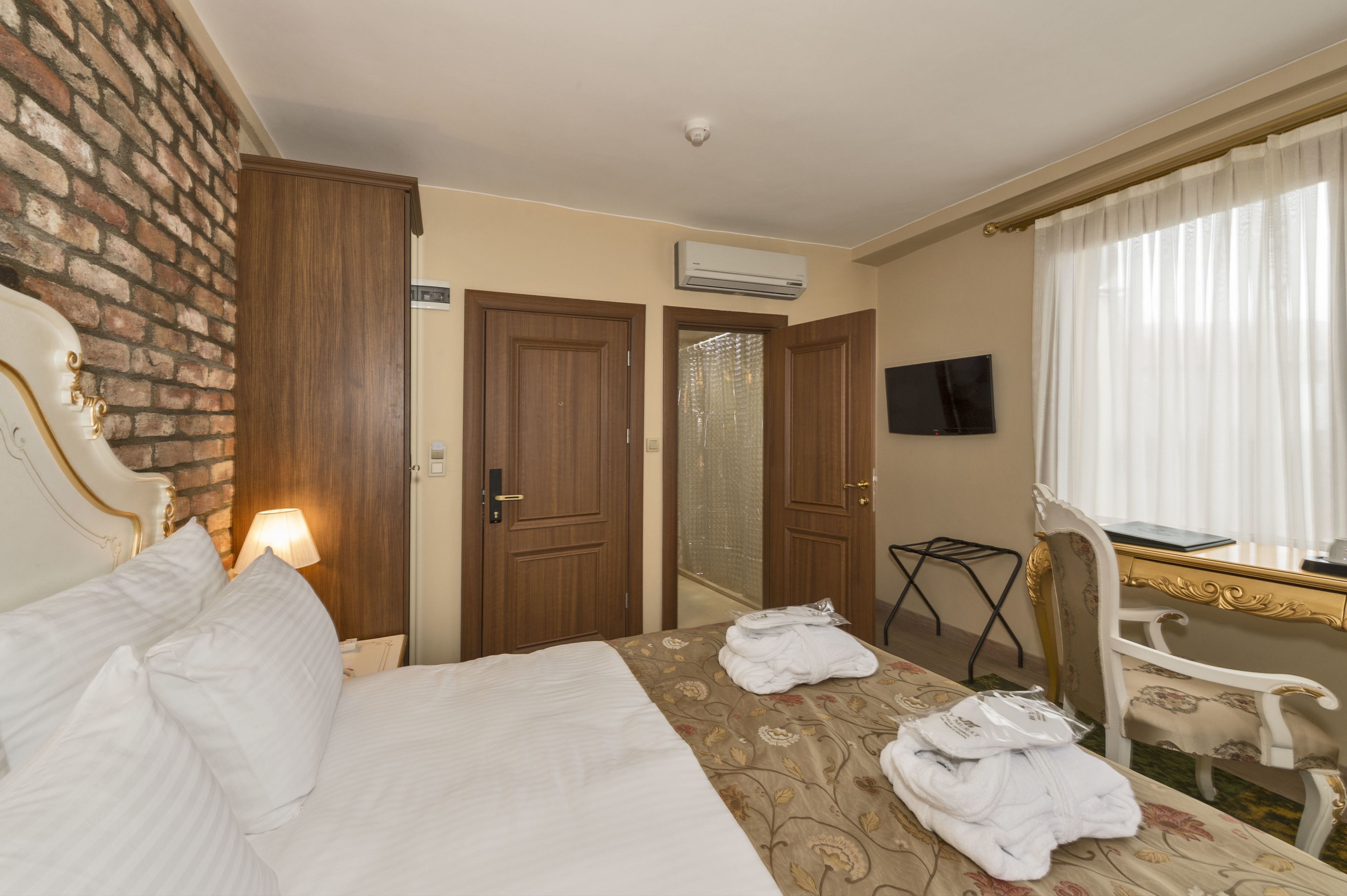 A hotel room with a bed, a desk, a chair, a TV, and an air conditioning unit.