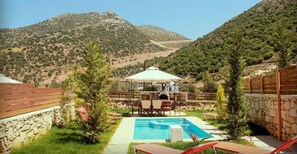 A pool area with a gazebo, surrounded by stone walls and greenery, overlooking a mountainous landscape.
