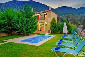 A two-story house with a swimming pool and lounge chairs.