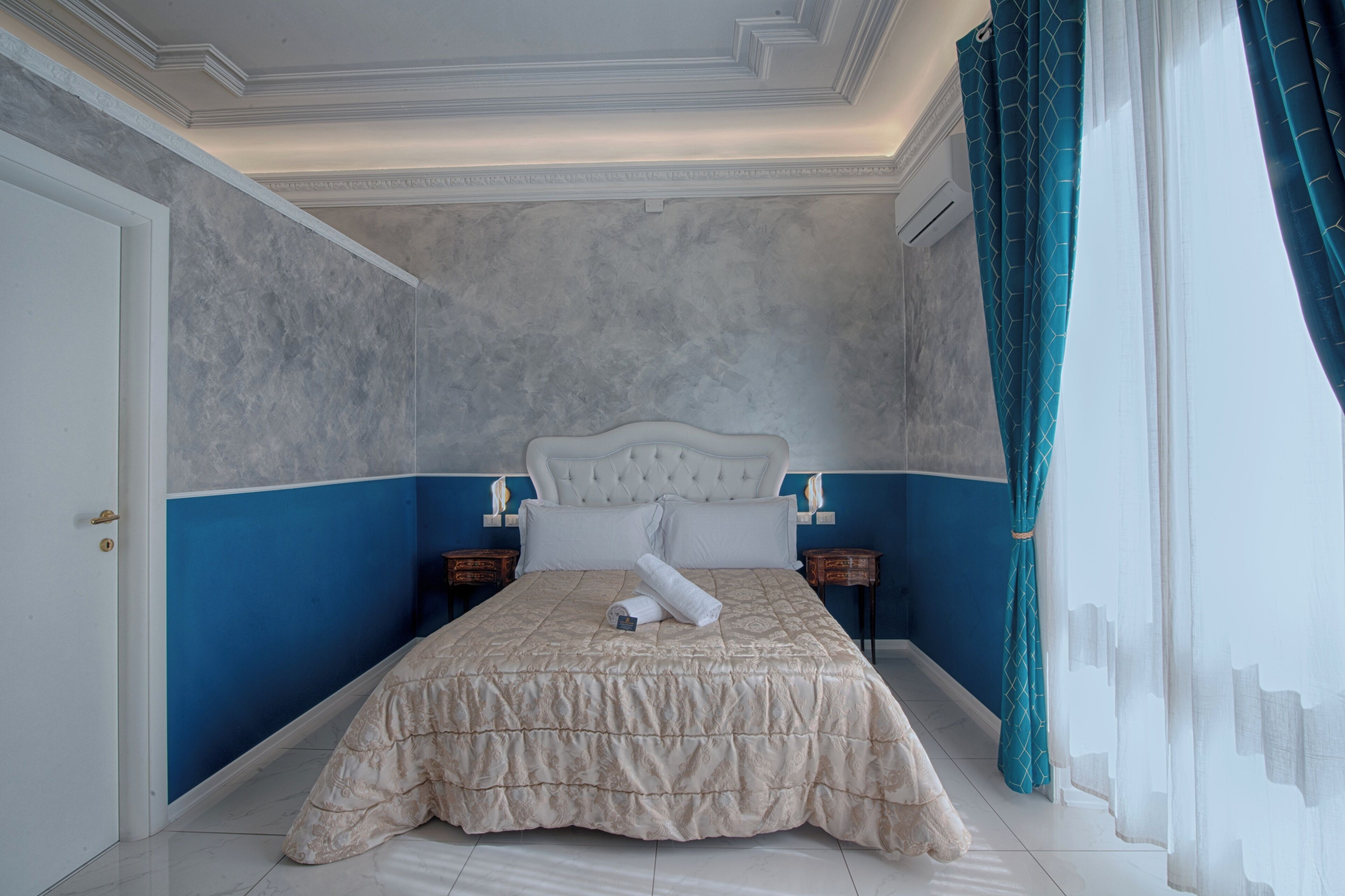 A bedroom with a large bed, a headboard, two bedside tables, and a window with curtains.