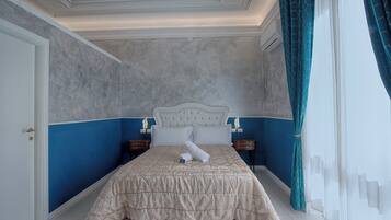 A bedroom with a large bed, a headboard, two bedside tables, and a window with curtains.