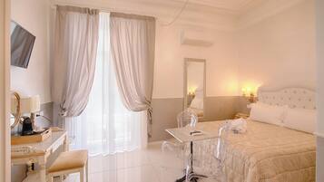 A hotel room with a bed, a desk with a chair, a vanity with a mirror, and a window with curtains.