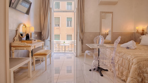 Habitación de hotel con cama, escritorio con silla, mesa con silla, espejo y vista al balcón.