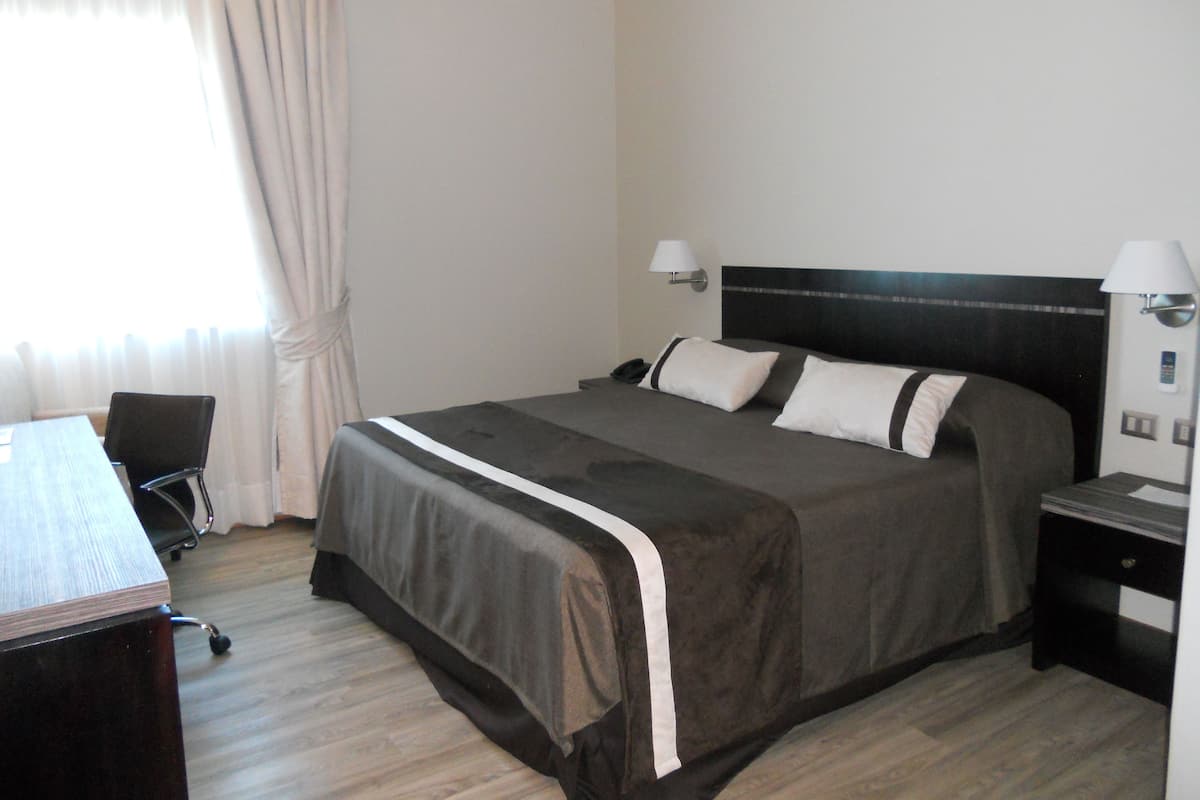Una habitació d'hotel amb un llit gran, un escriptori, una cadira, una làmpada i una tauleta de nit.