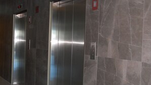 Dois elevadores em um corredor com paredes de mármore e chão de azulejos.