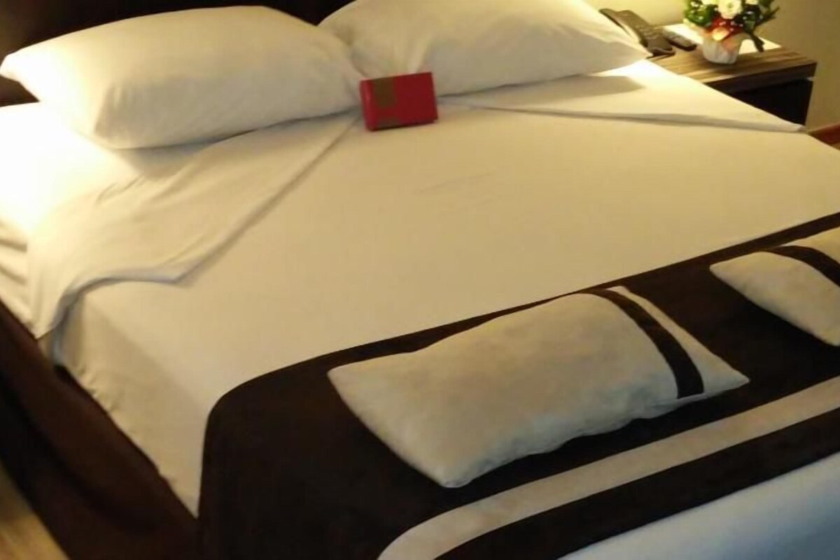 Un lit bien fait, avec une literie blanche et un coussin décoratif marron.