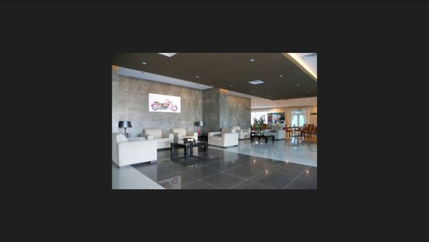 Um hall amplo com design moderno, apresentando uma grande área de estar com sofás e uma mesa de centro, uma obra de arte colorida fixada na parede, e um teto bem iluminado.