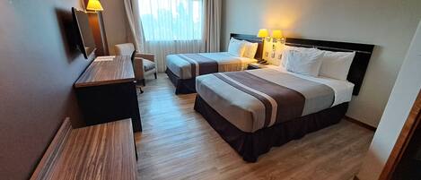 Habitación de hotel con dos camas, un escritorio, una silla y un ventanal con cortinas.