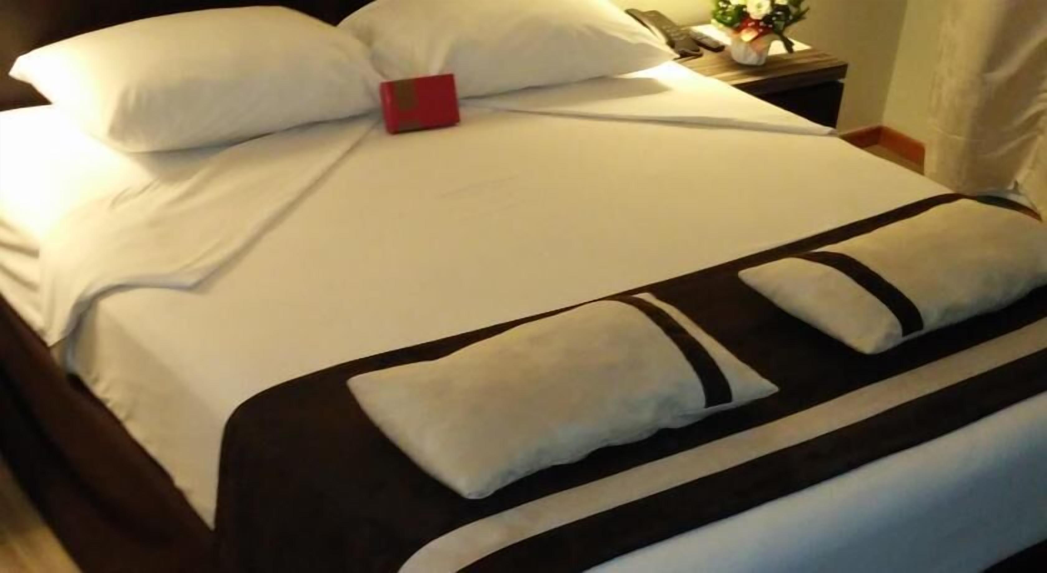 A neatly made bed with white bedding, a red accent pillow, and a brown and white striped blanket.