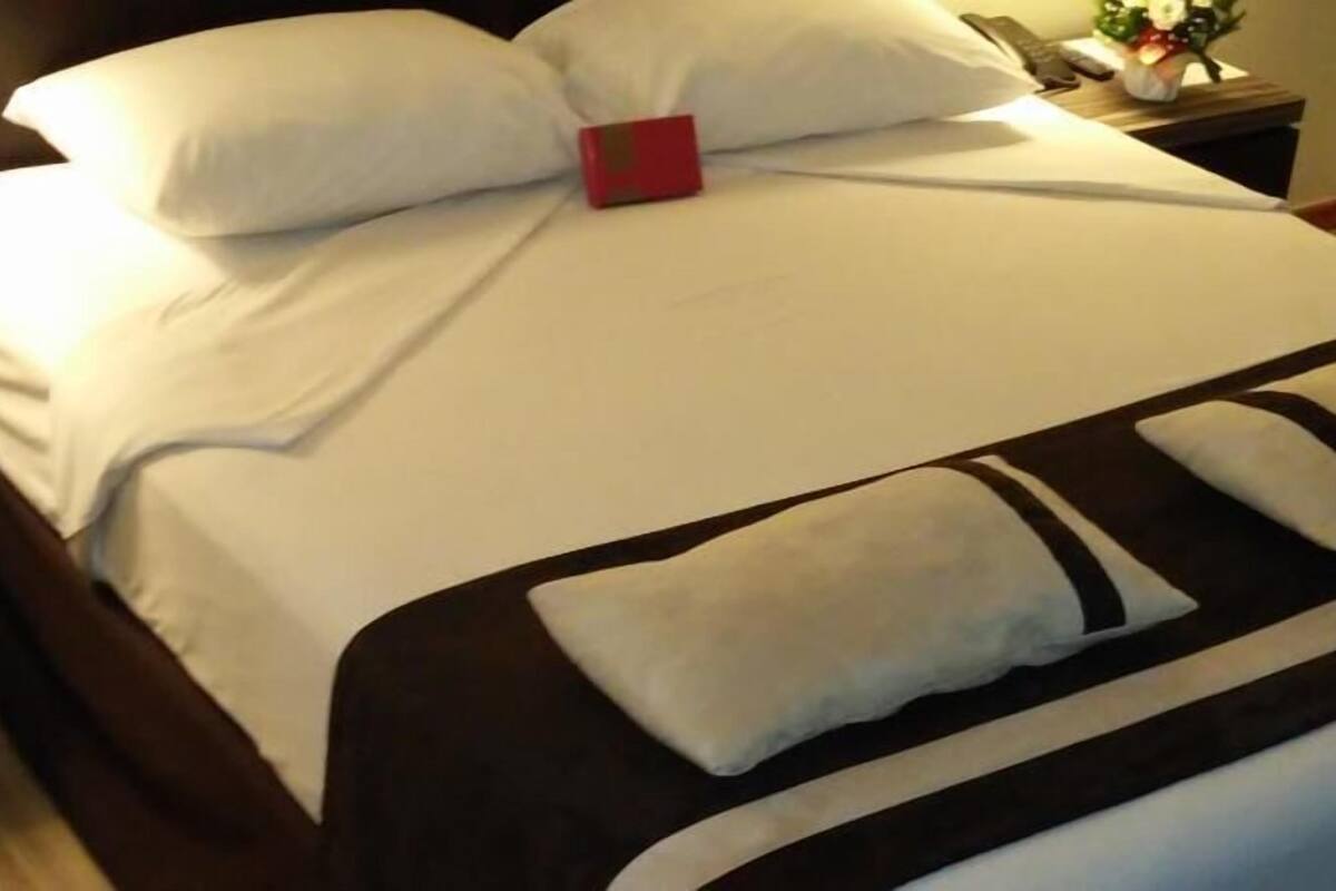 A neatly made bed with white bedding, a red accent pillow, and a brown and white striped blanket.