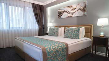 Habitación de hotel con una cama grande, dos lámparas de noche, un cuadro en la pared y una ventana con cortinas.