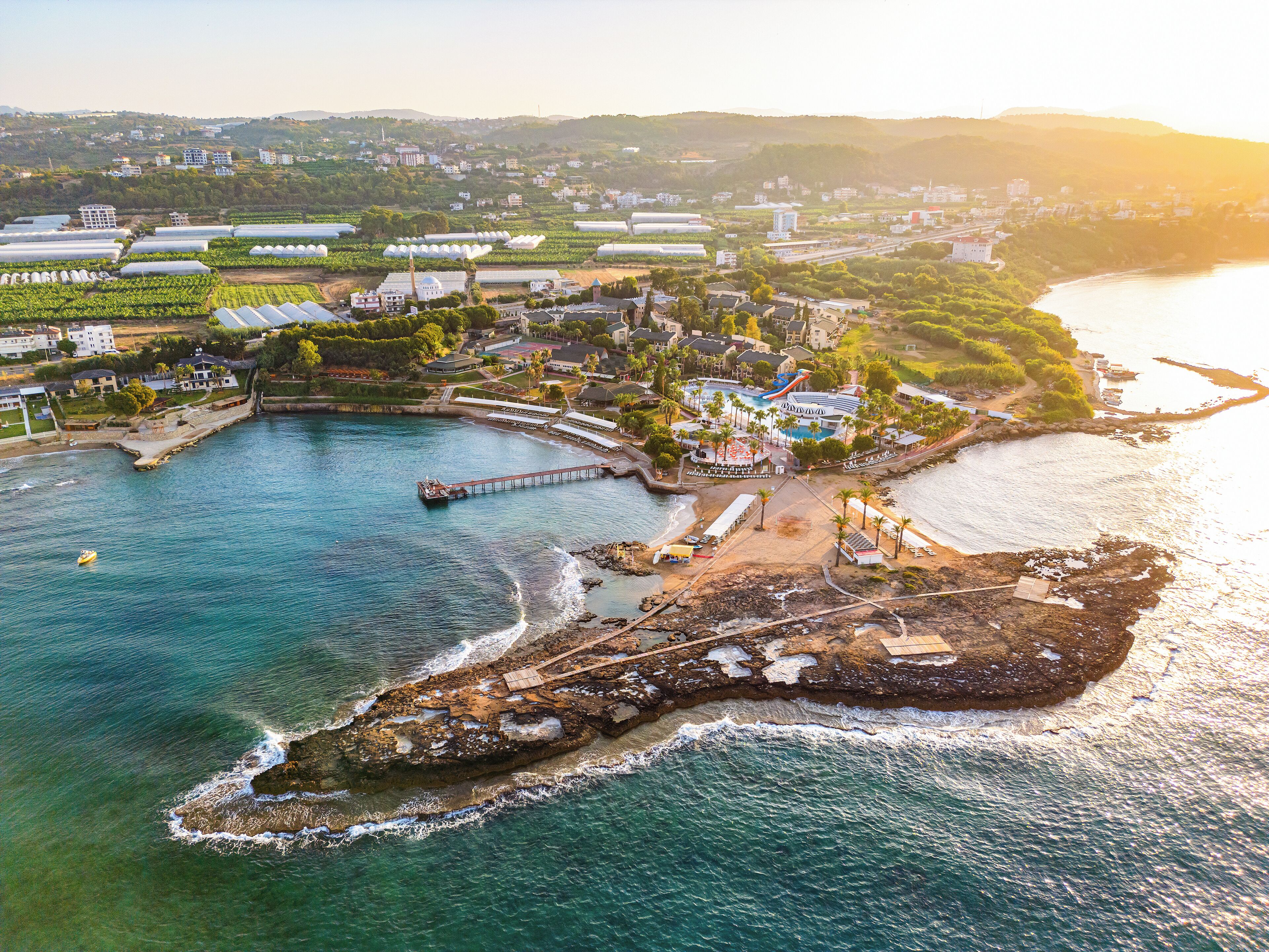 An aerial view of a coastal resort with a pier, beachfront villas, and a swimming pool area.