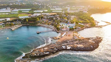 An aerial view of a coastal resort with a pier, beachfront villas, and a swimming pool area.