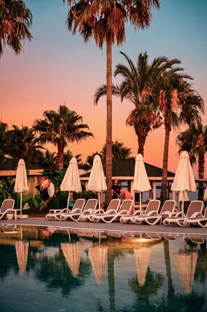 A poolside area with lounge chairs and umbrellas, surrounded by palm trees. - Oz Hotels İncekum Beach Resort (Alanya)