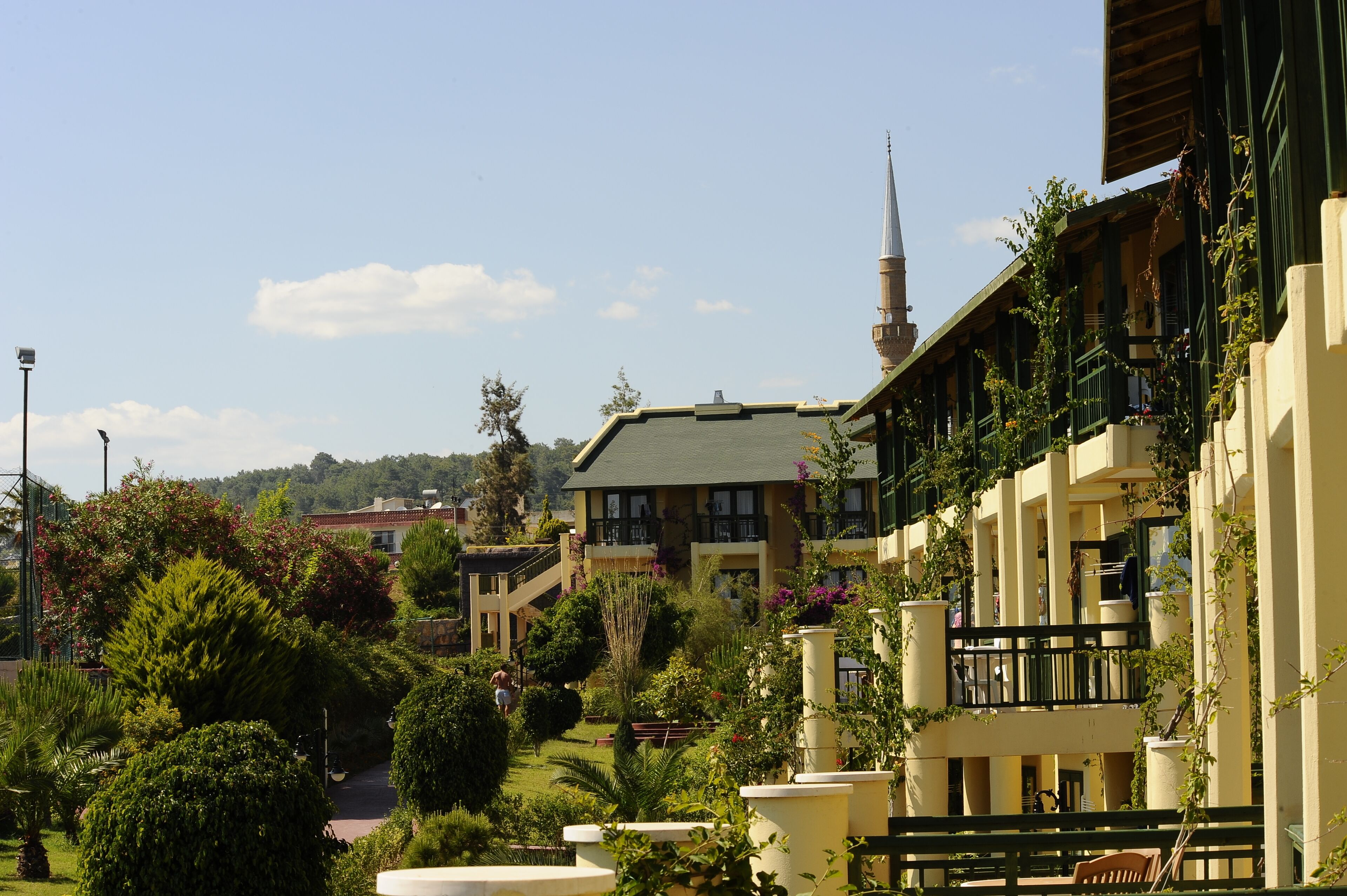 A hotel with a green roof, multiple balconies, and a garden area with various plants and a pathway.