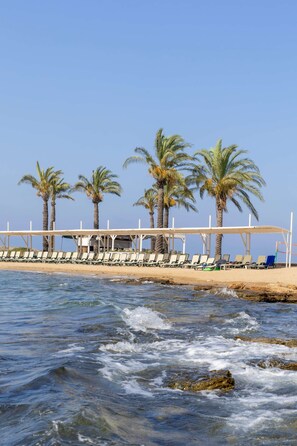 A beach with palm trees, a covered seating area, and a rocky shoreline. - Oz Hotels İncekum Beach Resort (Alanya)