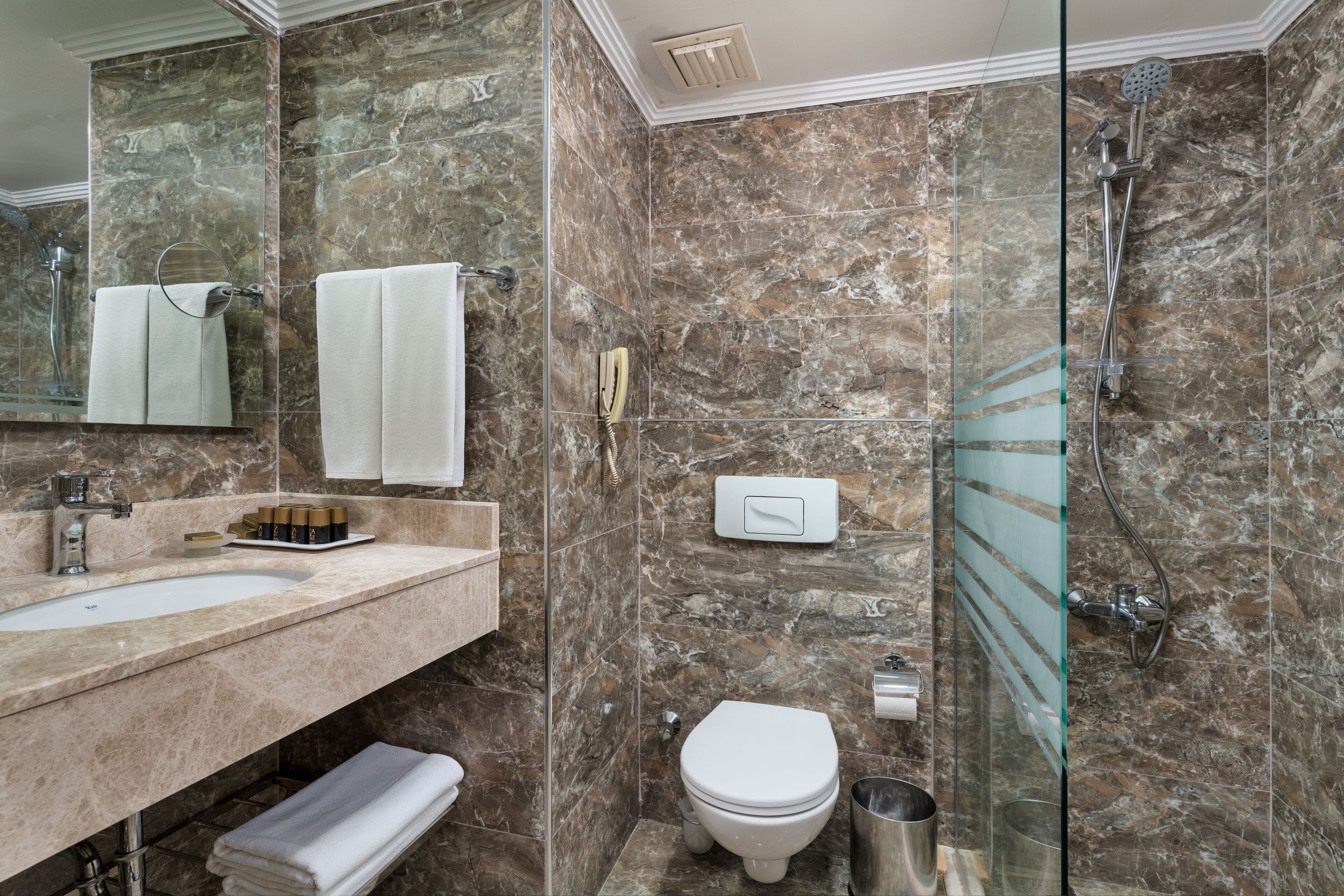A bathroom with a marble wall, a glass shower enclosure, a white sink, and a toilet.