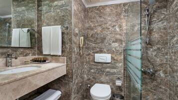 A bathroom with a marble wall, a glass shower enclosure, a white sink, and a toilet.