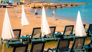 A beachside view with lounge chairs and umbrellas, a flag, and a rocky shoreline. - Oz Hotels İncekum Beach Resort (Alanya)
