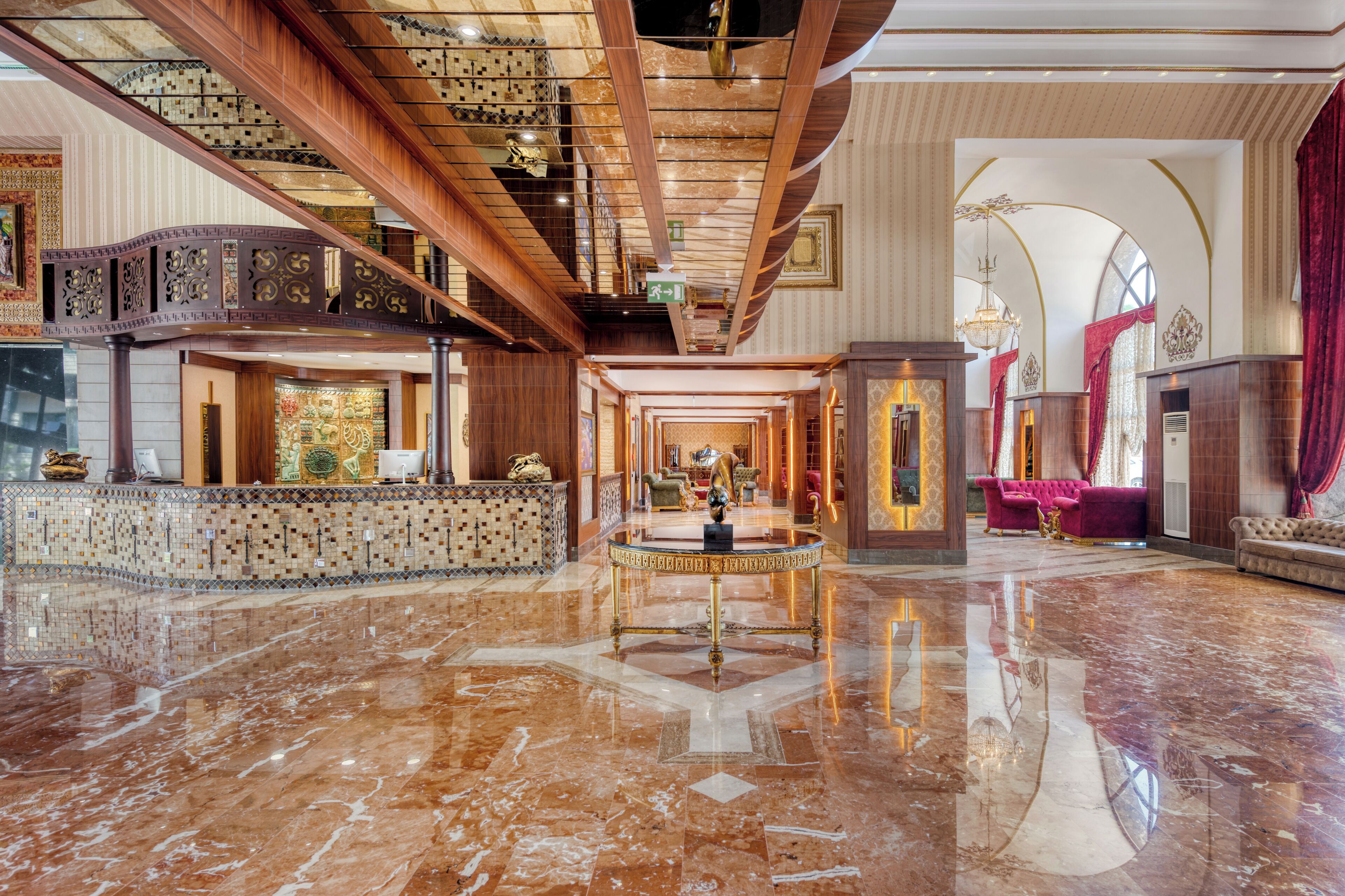 A spacious lobby with a marble floor, a central round table, and a staircase leading to an upper level.
