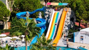 Parque aquático com diversas piscinas escorregadoras e área de piscina com espreguiçadeiras e guarda-sóis.