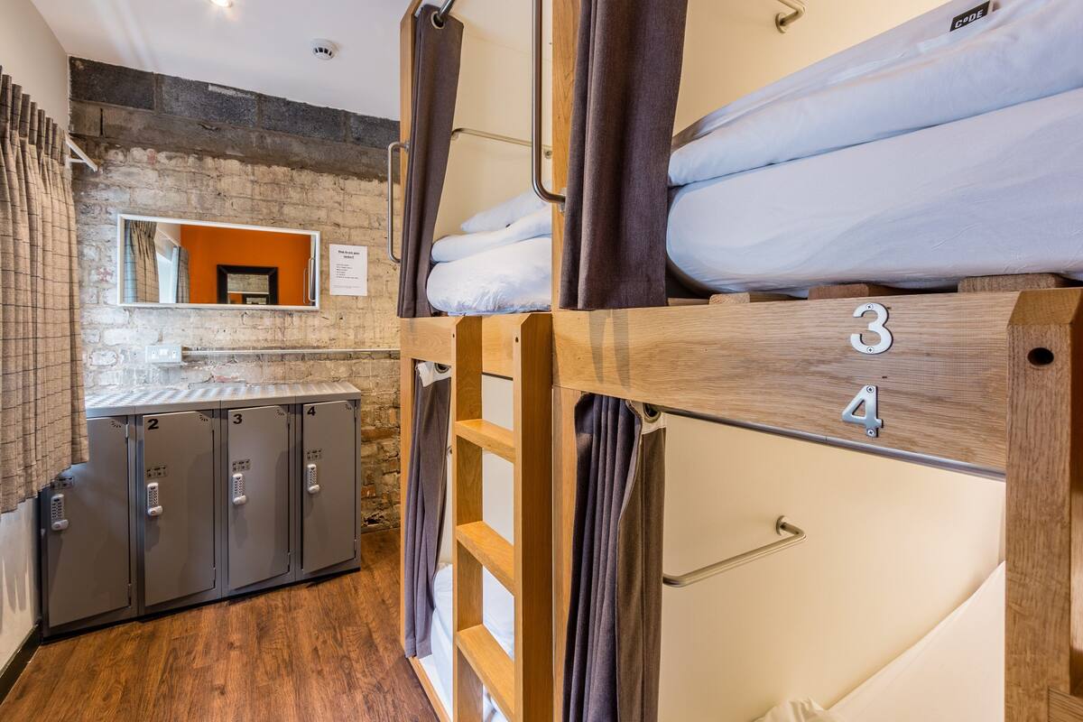 A dormitory-style room with bunk beds, numbered lockers, and a mirror.