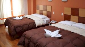 Quarto de hotel com duas camas, cada uma com roupa de cama marrom e almofadas brancas. Há uma mesa de cabeceira com um telefone e uma luminária de um lado.