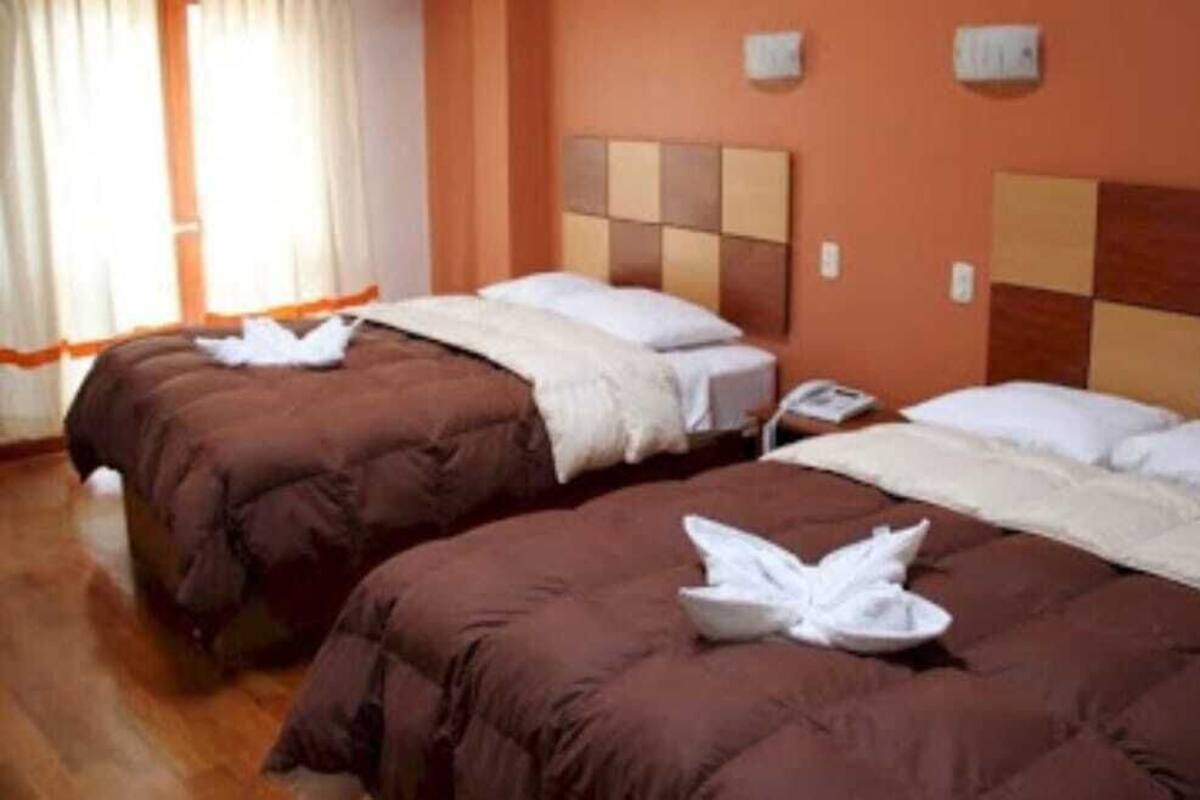 A hotel room with two beds, each with brown bedding and white pillows. There is a nightstand with a phone and a lamp on one side.
