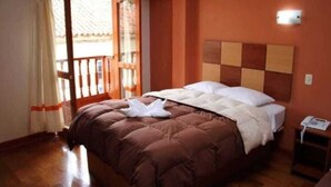Habitación de hotel con piso de madera, una cama con colcha marrón, almohada blanca y cabecera de madera.