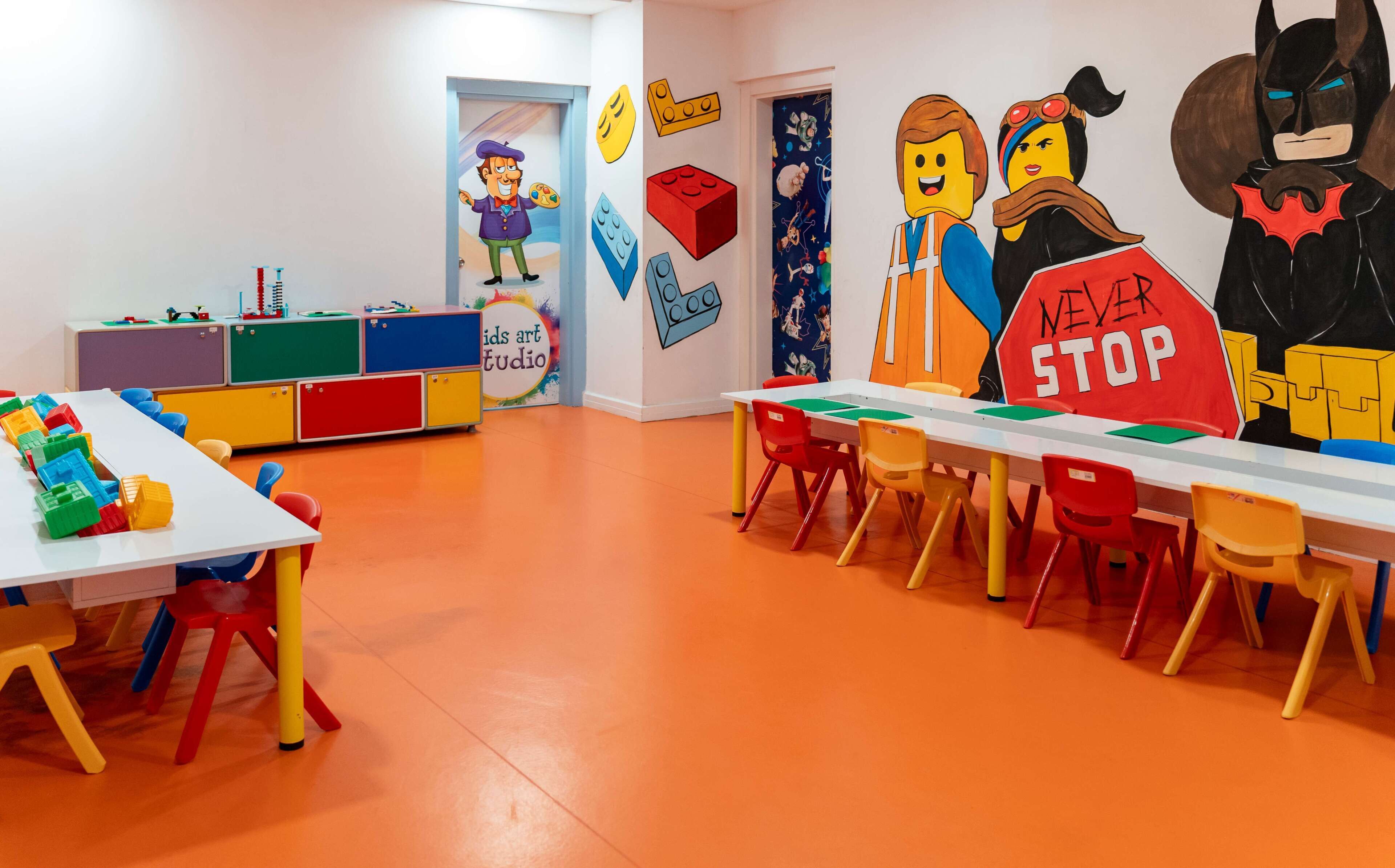 A children's art studio with colorful furniture and LEGO figures on the walls.