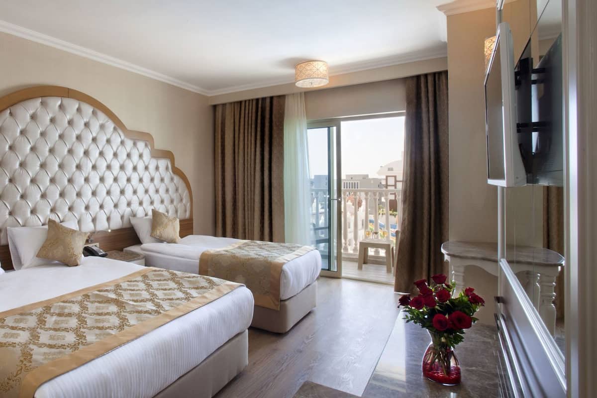Ein Hotelzimmer mit zwei Betten, einem großen, gepolsterten Kopfteil, einem Balkon mit Blick und einem Flachbildfernseher.