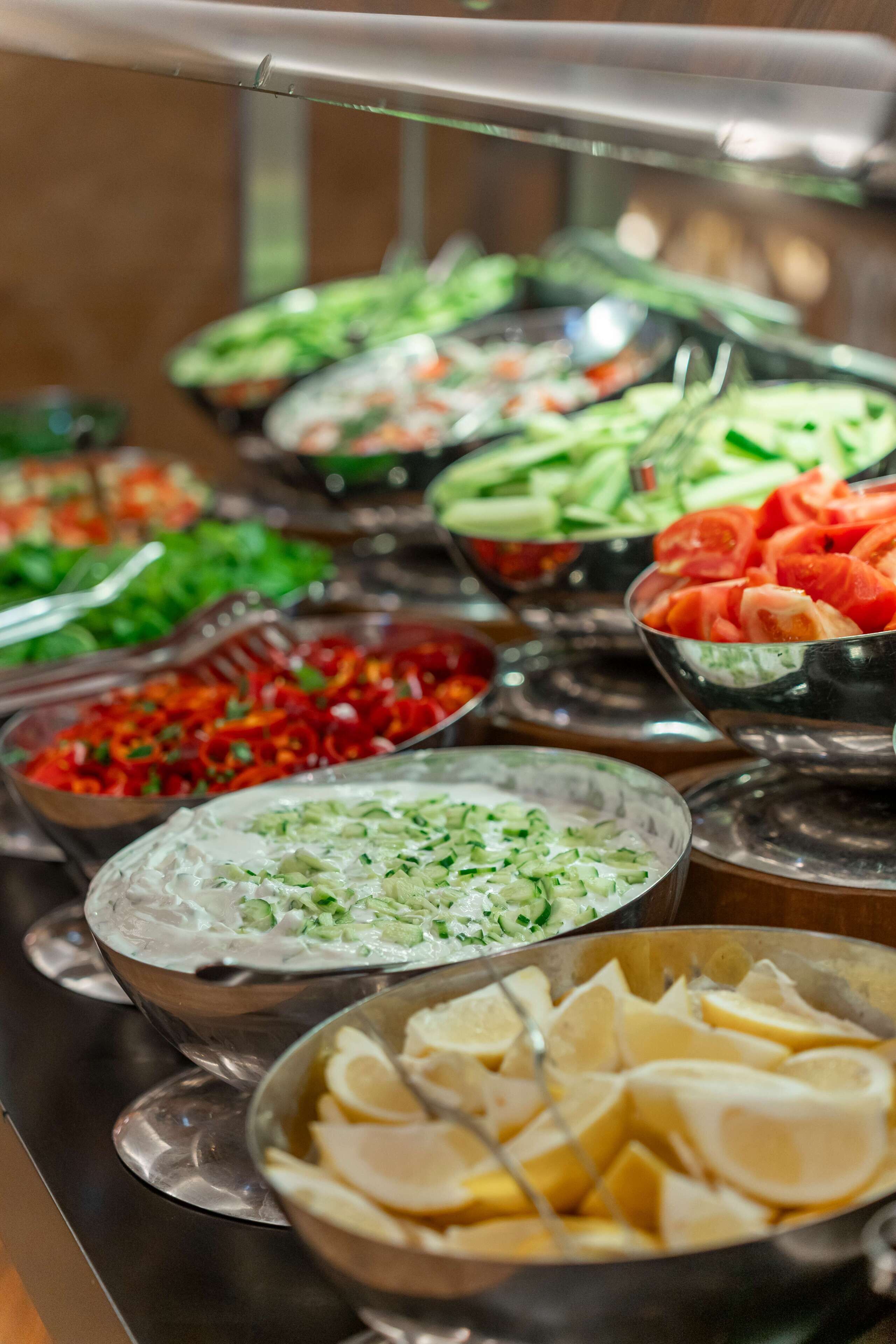 Un bufé con diversos alimentos, como ensaladas, verduras y carnes en rodajas.
