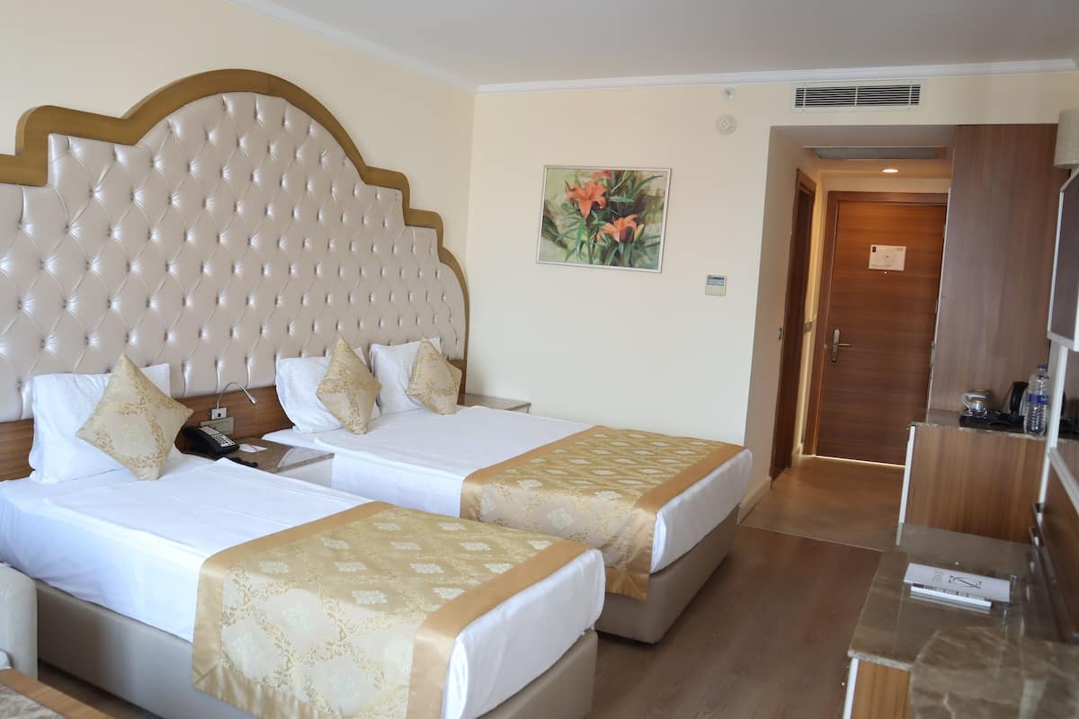 Ein Hotelzimmer mit zwei Betten, einem Holzkopfteil, einem Gemälde an der Wand und einer Holztür.