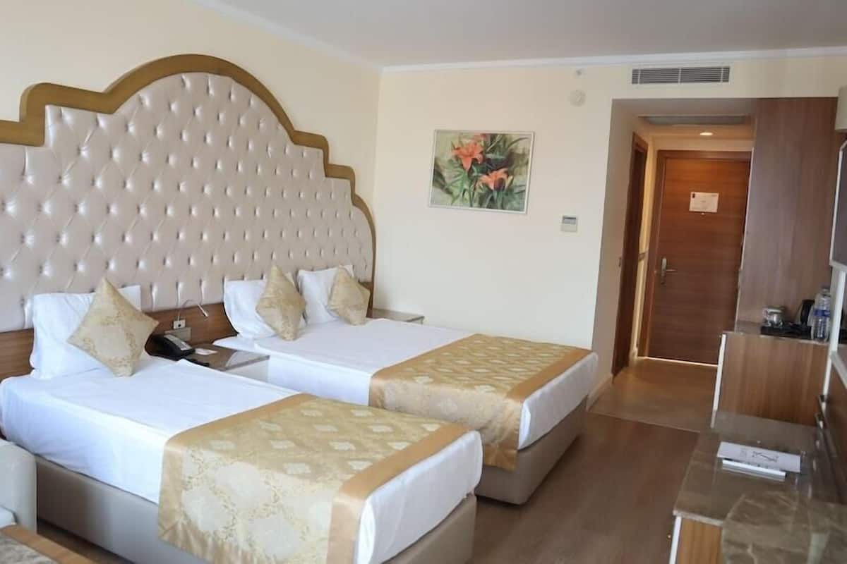 Ein Hotelzimmer mit zwei Betten, einem großen, gepolsterten Kopfteil, einem Bild an der Wand und einer Holztür.