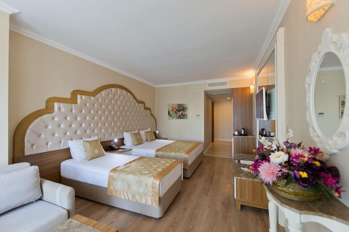 Ein Hotelzimmer mit zwei Betten, einem Schlafsofa, einem Schminktisch mit Spiegel und einer Blumenkomposition.