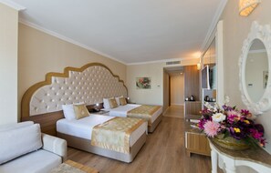 A hotel room with two beds, a sofa, a vanity with a mirror, and a floral arrangement. - Oz Hotels Side Premium (Manavgat)