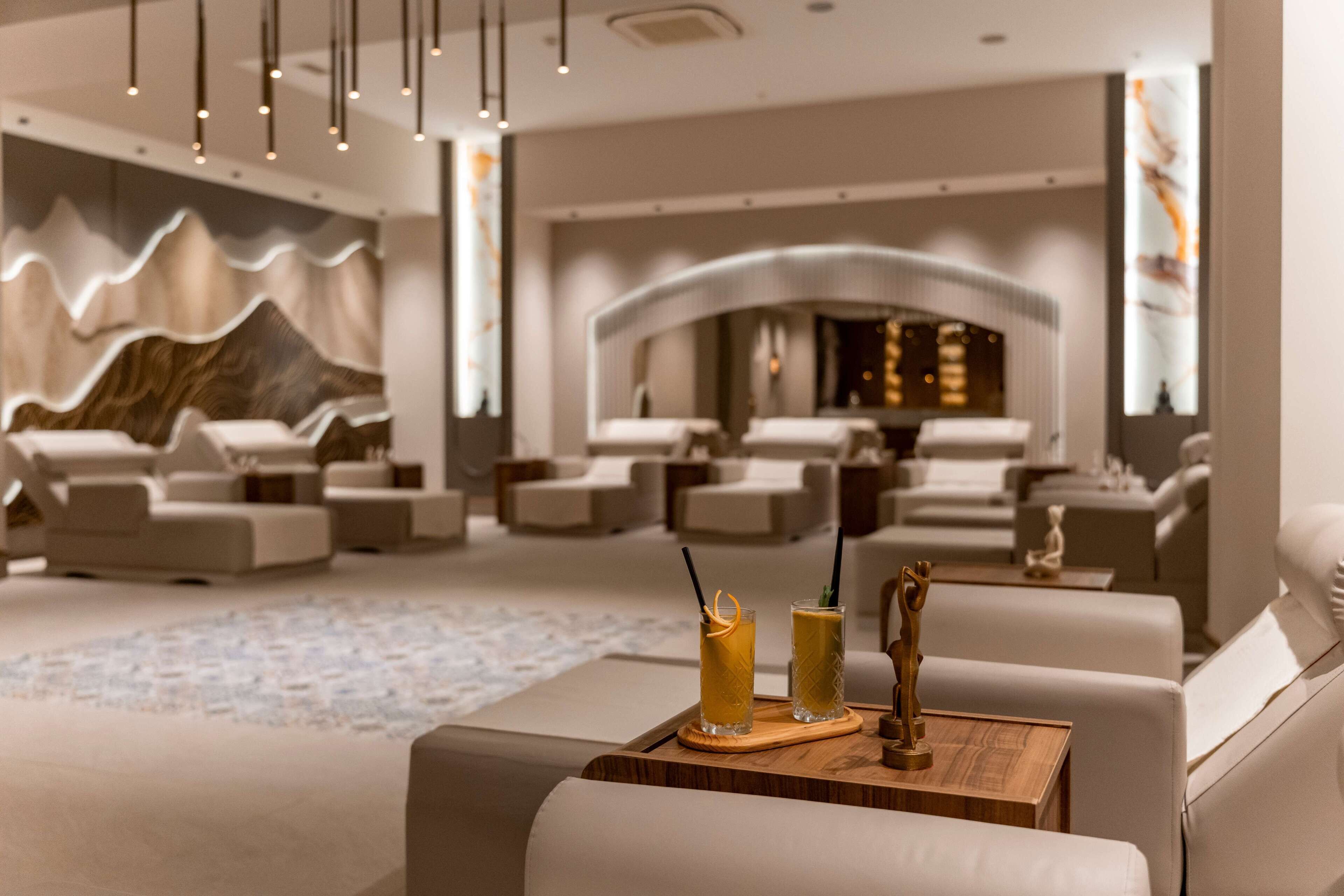 A modern lounge area with sofas, a wooden table with drinks, and a decorative wall.