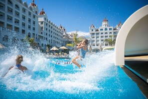 A swimming pool with water splashing, surrounded by hotel buildings with domed roofs. - Oz Hotels Side Premium (Manavgat)