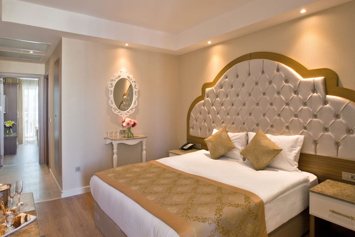 Ein Hotelzimmer mit einem großen Bett, einem Nachttisch, einem Spiegel und Blick auf einen Flur.
