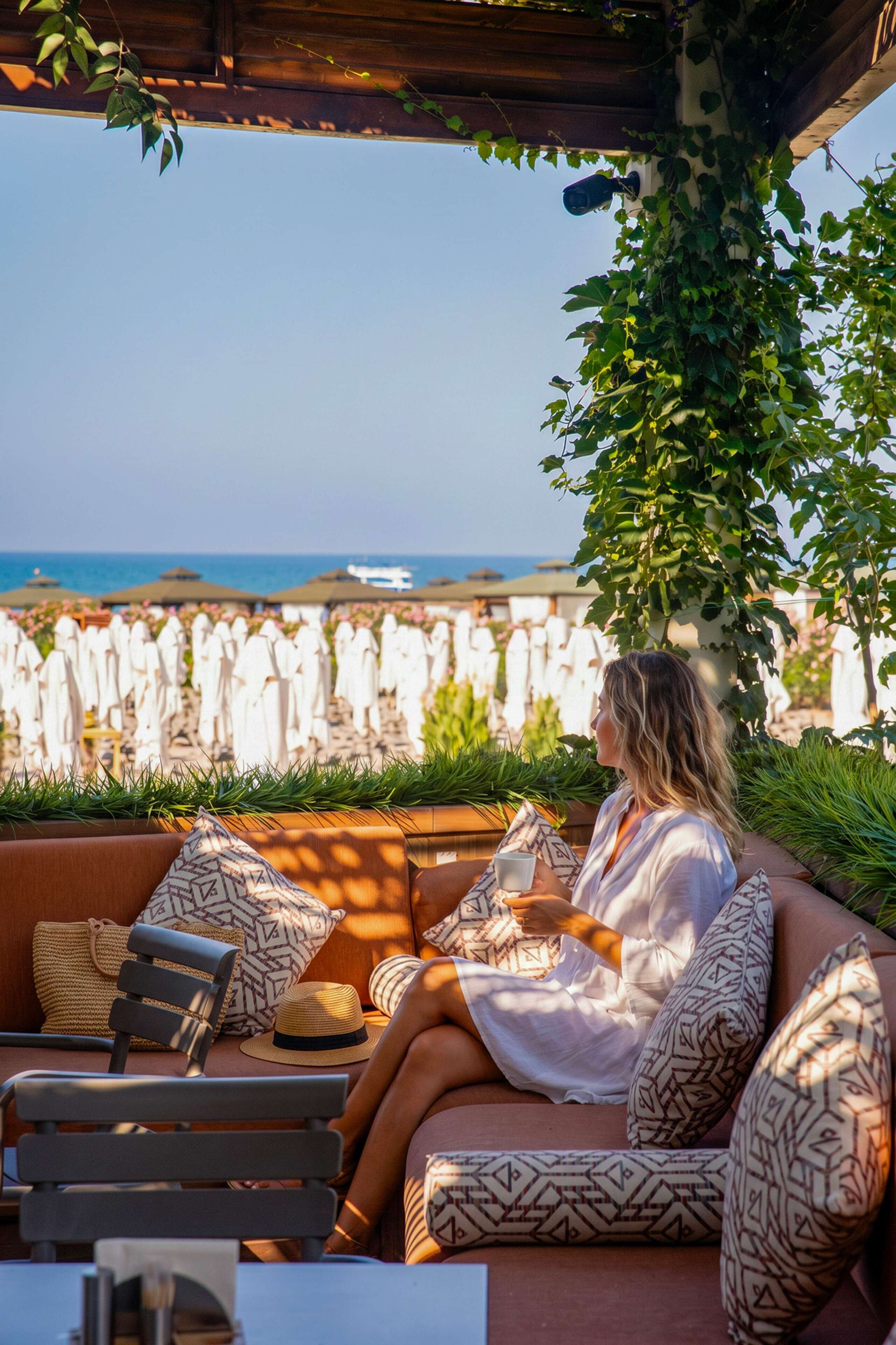 A person seated on a cushioned outdoor sofa with a view of the sea and a stone wall in the background.