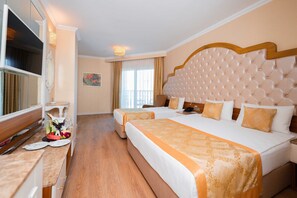 A hotel room with two beds, a TV, a desk with a fruit basket, and a painting on the wall. - Oz Hotels Side Premium (Manavgat)