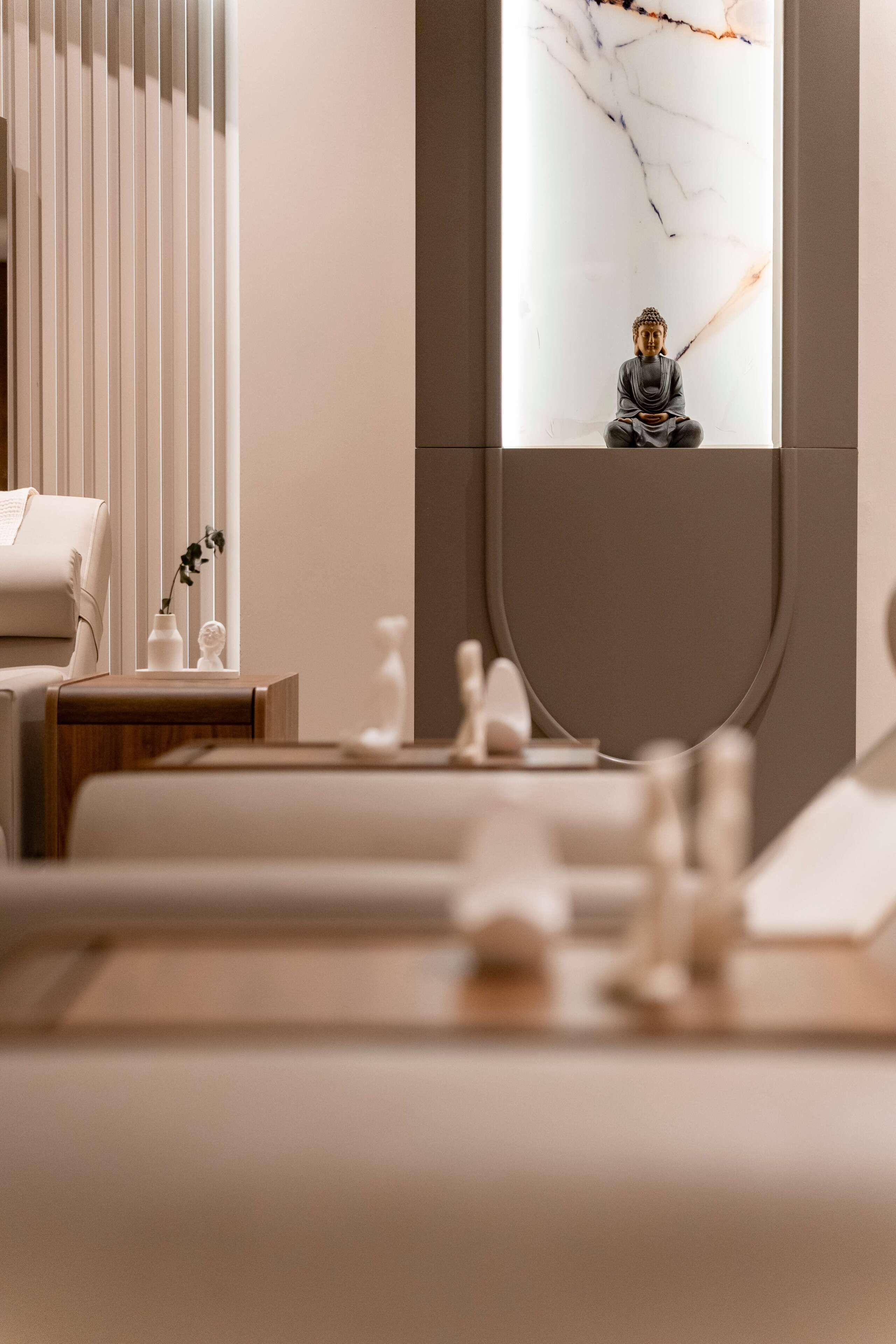 Ein modernes Interieur mit minimalistischem Design, das ein Sofa, einen kleinen Tisch mit einer Vase und einer Statue sowie eine Buddha-Statue in einer Nische zeigt.