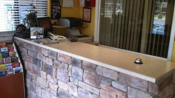 A reception desk with a stone facade, a computer, and a plant. - Orange City Motel (Orange City)