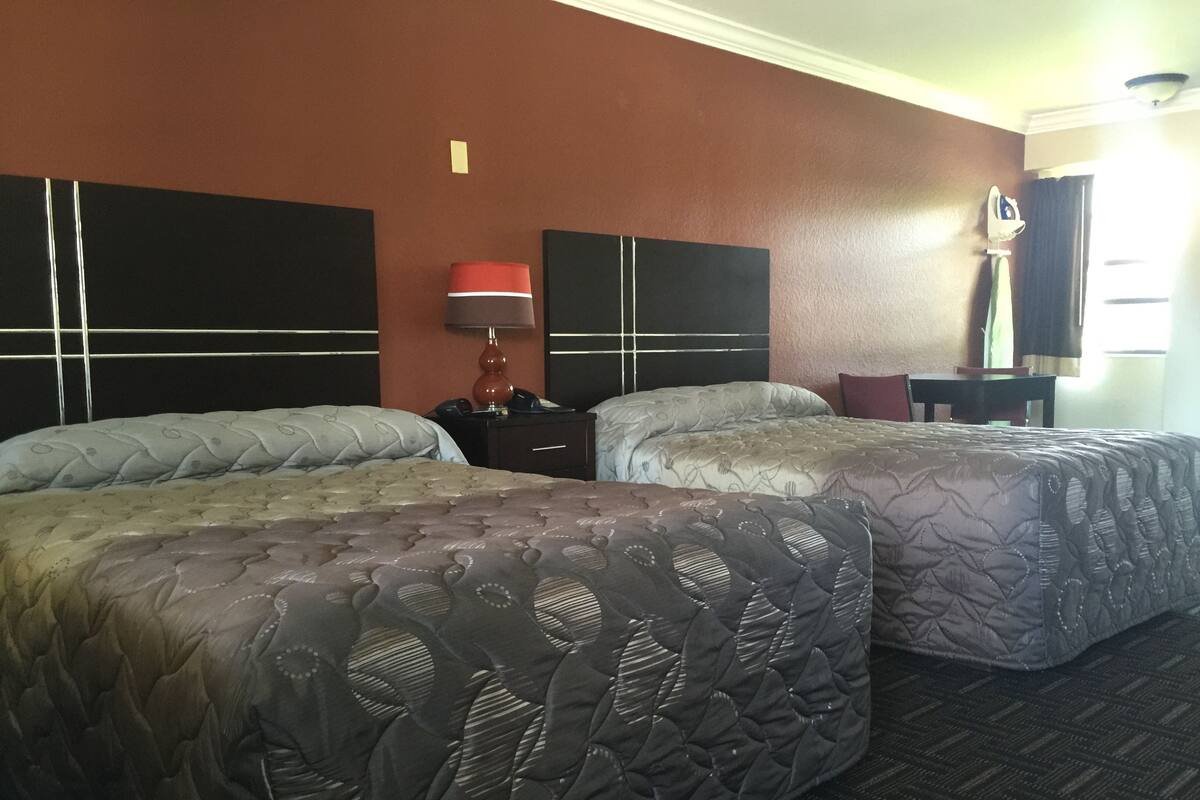 Ein Hotelzimmer mit zwei Betten, einem Nachttisch, einer Lampe, einem Schreibtisch und einem Stuhl.