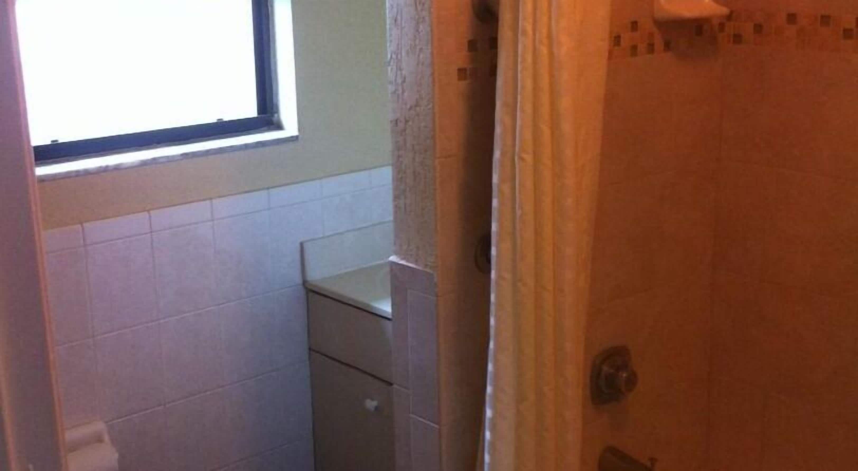 A bathroom with white tiled walls, a window, and a shower area.