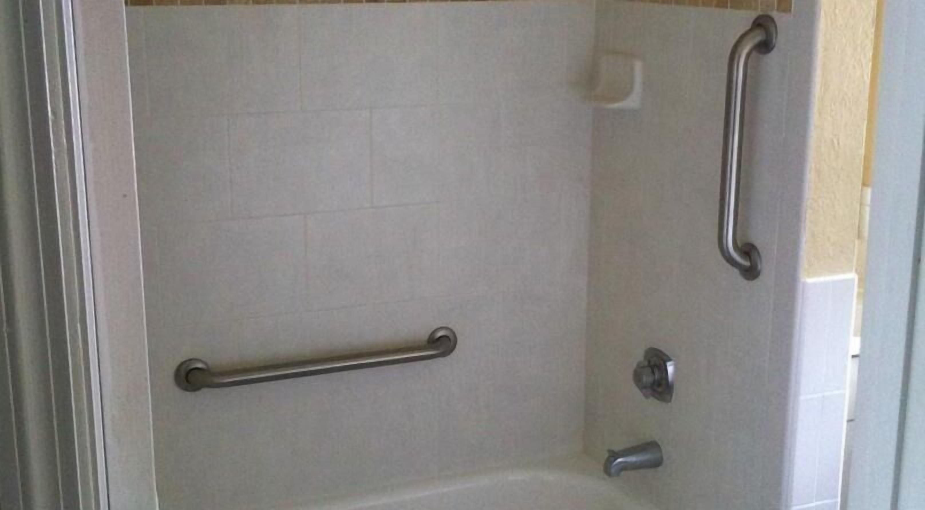 A bathroom with a bathtub, a handrail, and a shower control panel.