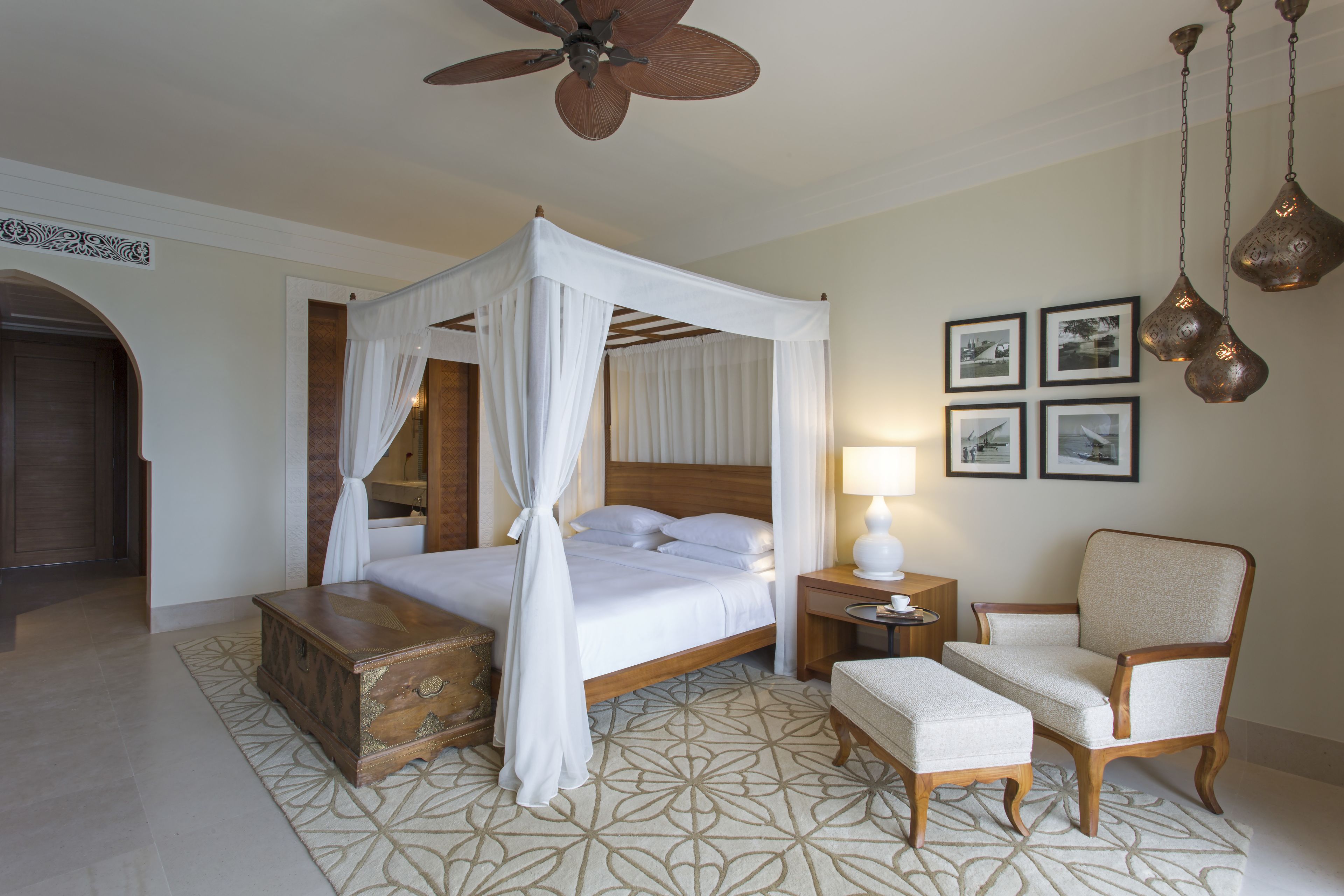 A bedroom with a four-poster bed, a wooden nightstand, a chair, and a ceiling fan.